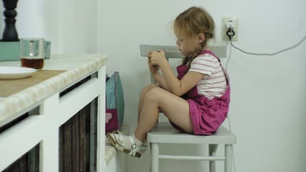 Meisje dat op de stoel zit, probeert te spelen van een spel met haar smartphone. Kind met behulp van mobiele telefoon — Stockvideo