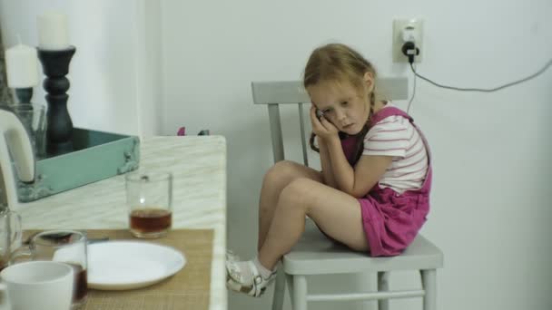 椅子に座っている小さな女の子が彼女のスマート フォンでゲームをプレイしようとするとします。子供の携帯電話を使用して — ストック動画
