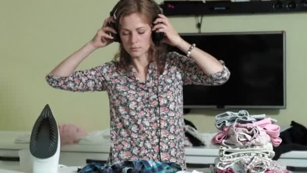 Mujer planchando la montaña de lavandería en casa en la cocina escuchando música en los auriculares y bailando — Vídeo de stock