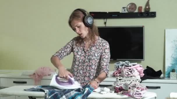 Mulher engomar a montanha de lavanderia em casa na cozinha ouvir música em fones de ouvido e dança — Vídeo de Stock