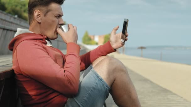 Reifer Mann, Tourist mit Smartphone, sitzt am Strand auf einer Holzbank — Stockvideo