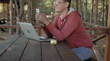 Olgun adam çalışıyor onun laptop üzerinde açık havada doğa onun meslek sırasında büyük tahta masada otururken kontrol e-posta için kendi dizüstü kullanarak forester yaşında.