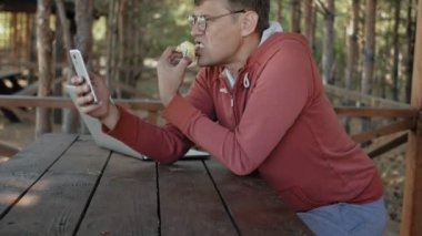 Olgun adam çalışıyor onun laptop üzerinde açık havada doğa onun meslek sırasında büyük tahta masada otururken kontrol e-posta için kendi dizüstü kullanarak forester yaşında.