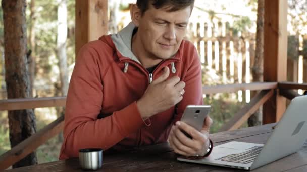 Uomo maturo sta lavorando sul suo computer portatile all'aperto in natura durante la sua vocazione forestale invecchiato utilizzando il suo computer portatile per il controllo e-mail mentre seduto a un enorme tavolo di legno — Video Stock