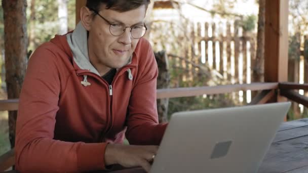 Mature man is working on his laptop outdoors in nature during his vocation aged forester using his laptop for e-mail checking while sitting at huge wooden table — Stock Video