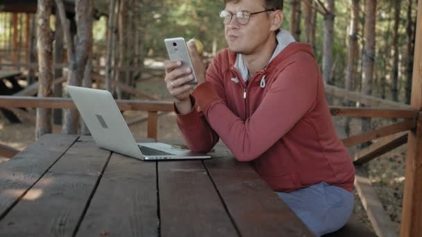 Uomo maturo sta lavorando sul suo computer portatile all'aperto in natura durante la sua vocazione forestale invecchiato utilizzando il suo computer portatile per il controllo e-mail mentre seduto a un enorme tavolo di legno — Video Stock