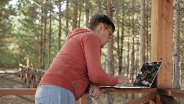 Uomo maturo sta lavorando sul suo computer portatile all'aperto in natura durante la sua vocazione forestale invecchiato utilizzando il suo computer portatile per il controllo e-mail mentre seduto a un enorme tavolo di legno — Video Stock