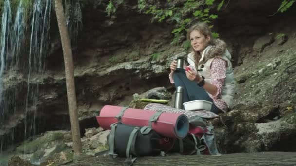 Mooie jongedame toeristische zittend op stilstand in bos. Mooie brunette toeristische meisje zit in het bos in de buurt van haar rode rugzak. , Herfst toerisme concept — Stockvideo