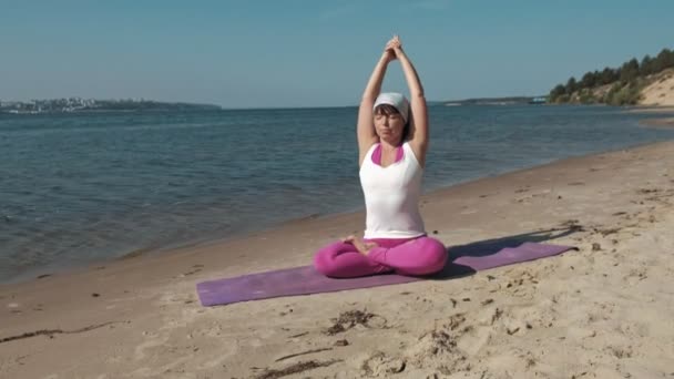 Oude gepensioneerde vrouw doet wat yoga op het strand — Stockvideo