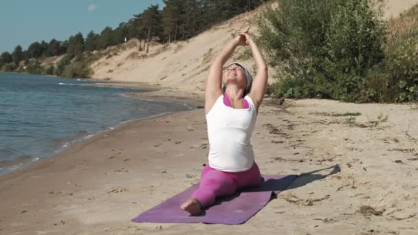 Vecchia donna in pensione facendo un po 'di yoga sulla spiaggia — Video Stock