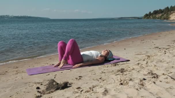 Oude gepensioneerde vrouw doet wat yoga op het strand — Stockvideo