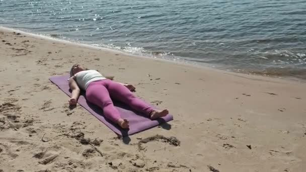 Old retired woman doing some yoga on the beach — Stock Video