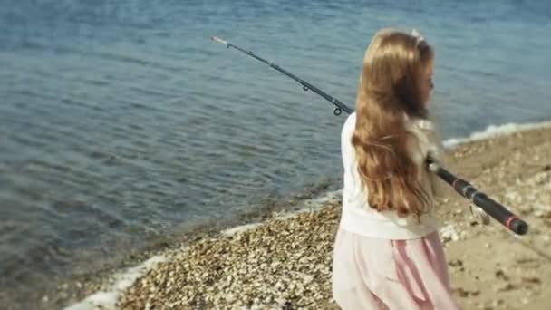 Carina bambina sta giocando con una canna da pesca su una barca da pesca vicino al fiume — Video Stock