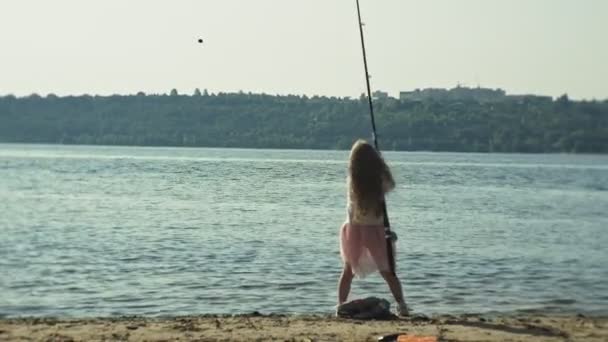 Menina bonito está brincando com uma vara de pesca em um barco de pesca perto do rio — Vídeo de Stock