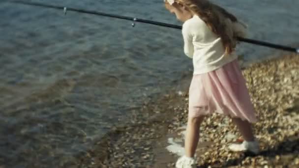 Menina bonito está brincando com uma vara de pesca em um barco de pesca perto do rio — Vídeo de Stock