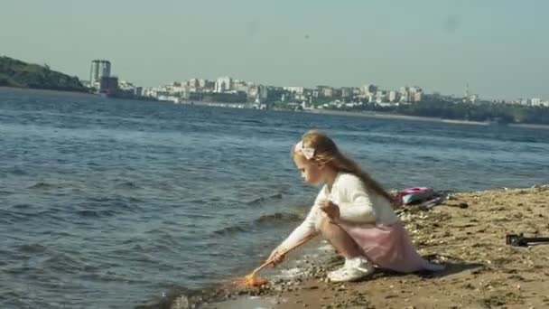 Une petite fille douce attrape des insectes avec un filet vert dans l'allée à côté de la rivière par une journée d'été ensoleillée — Video