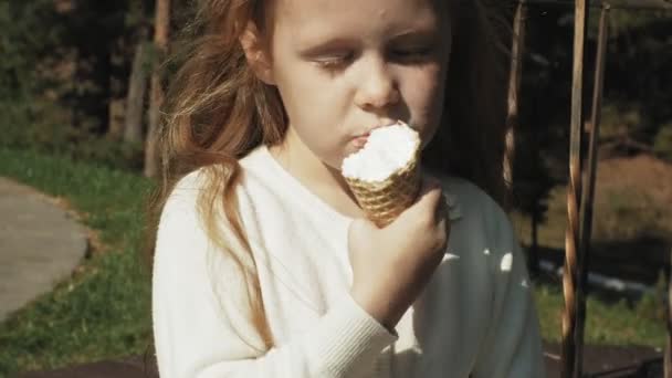 Симпатичная девушка сидит в парке и ест мороженое — стоковое видео