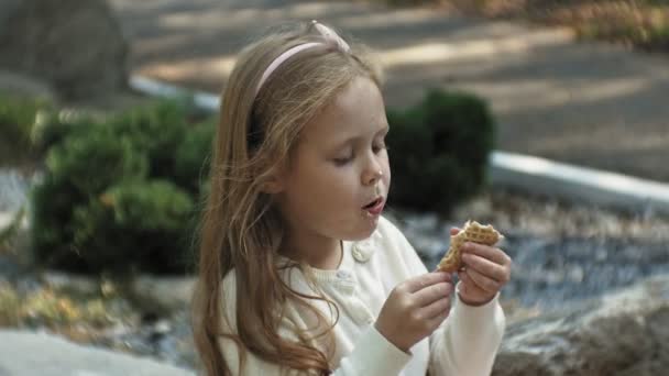 Egy aranyos lány ül a parkban, és eszik fagylaltot — Stock videók