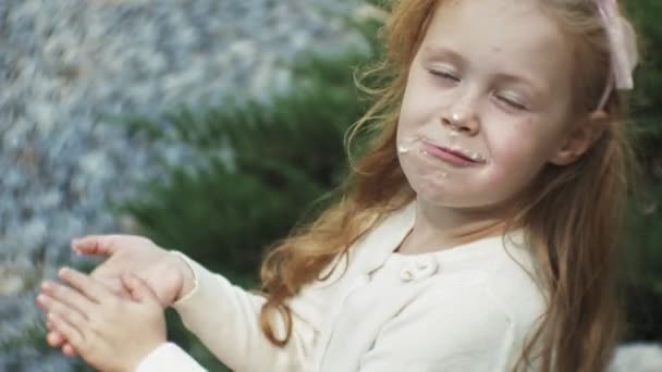 Una linda chica está sentada en el parque y comiendo helado — Vídeos de Stock