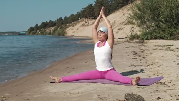 Old retired woman doing some yoga on the beach — Stock Video