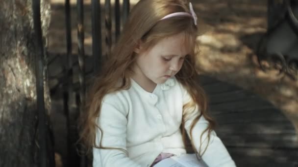 Uma menina doce senta-se na floresta e lê um livro — Vídeo de Stock