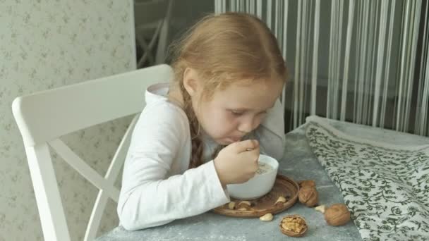 Kleines süßes Mädchen isst Haferflocken mit Nüssen und Trockenfrüchten zum Frühstück. gesundes Ernährungskonzept — Stockvideo