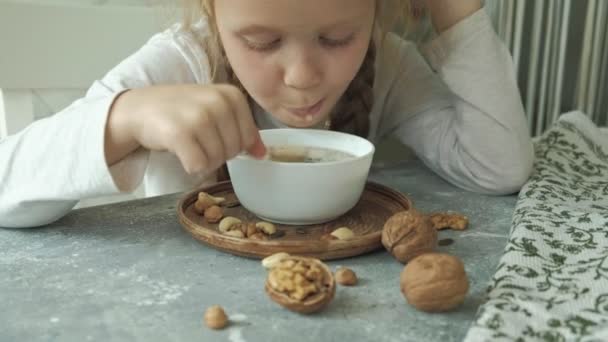 Το μικρό χαριτωμένο κορίτσι τρώει πλιγούρι βρώμης με ξηρούς καρπούς και αποξηραμένα φρούτα για πρωινό. Έννοια της υγιεινής διατροφής — Αρχείο Βίντεο
