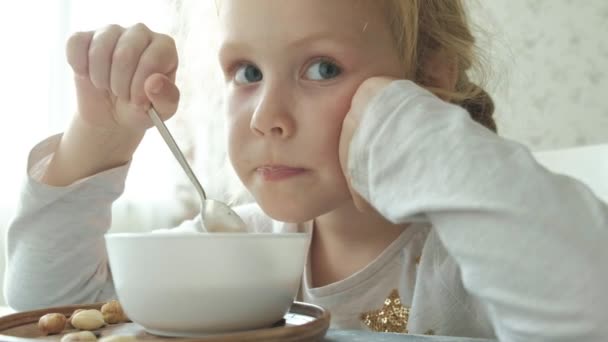 Menina bonito come aveia com nozes e frutas secas para o café da manhã. Conceito de alimentação saudável — Vídeo de Stock