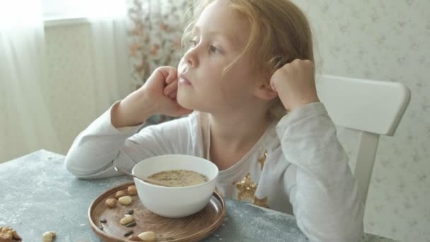 Malá roztomilá holčička jí ovesná kaše s oříšky a sušené ovoce na snídani. Zdravé jídlo koncept — Stock video