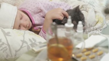 Hasta kız bir sıcaklık. Ateş bir çocukla bir kedi ile yatakta yatıyor.