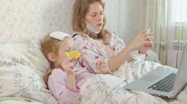 Hasta kız bir sıcaklık. Ateşli çocuk annesiyle yatakta yalan, meyve yemek yiyor ve bir dizüstü bilgisayar kullanarak.