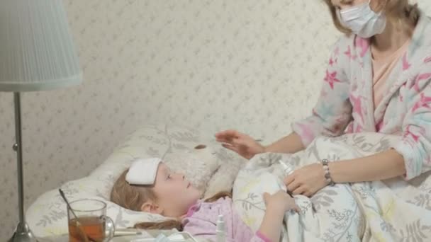 Sick girl with fever. Child with fever: a woman caring for a child and medicating — Stock Video