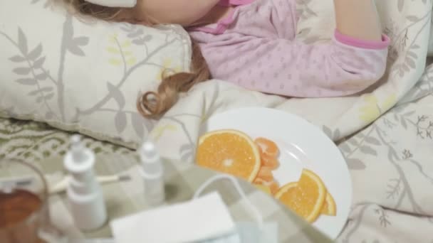 Niña enferma con fiebre. Un niño con fiebre se acuesta en la cama y come fruta. . — Vídeo de stock