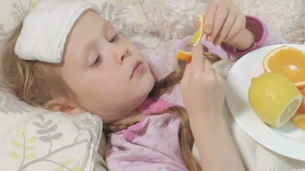 Fille malade avec fièvre. Un enfant qui a de la fièvre se couche et mange des fruits . — Video