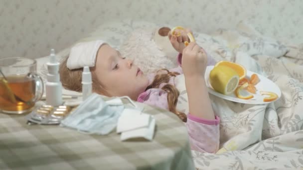 Beteg lány láz. A gyermek láz fekszik az ágyban, és eszik gyümölcsöt. — Stock videók