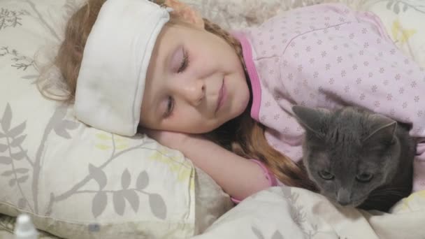 Sick girl with a temperature. A child with fever is lying in bed with a cat. — Stock Video