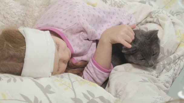 Nemocná dívka s teplotou. Dítě s horečkou leží v posteli s kočkou. — Stock video
