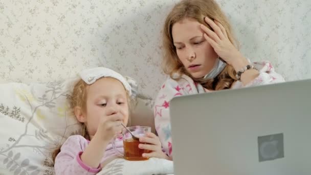 Niña enferma con temperatura. El niño con fiebre está acostado en la cama con su madre, comiendo fruta y usando una computadora portátil . — Vídeo de stock