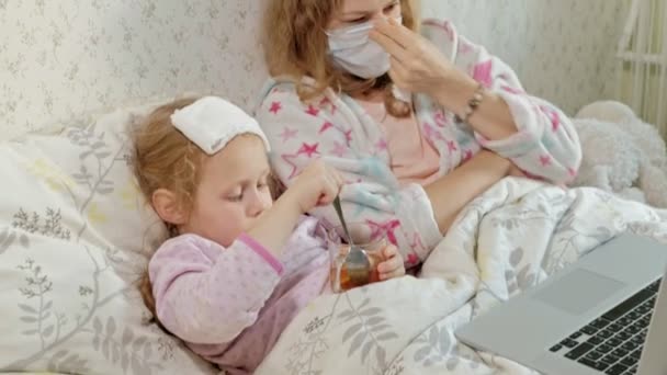 Beteg lány a hőmérséklet. Gyermek, lázzal feküdt az ágyban, az anyjával, eszik gyümölcsöt és használ egy laptop. — Stock videók