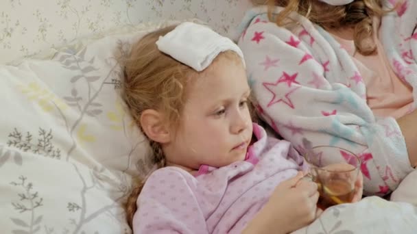 Menina doente com uma temperatura. Criança com febre está deitada na cama com a mãe, comendo frutas e usando um laptop . — Vídeo de Stock