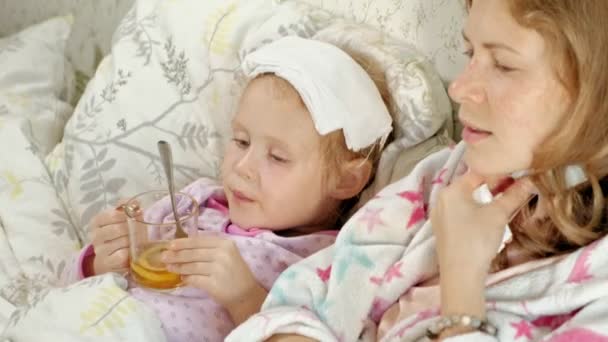 Chora dziewczyna z temperaturą. Dzieci z gorączką jest leżenie w łóżku ze swoją matką, jedzenie owoców i za pomocą laptopa. — Wideo stockowe