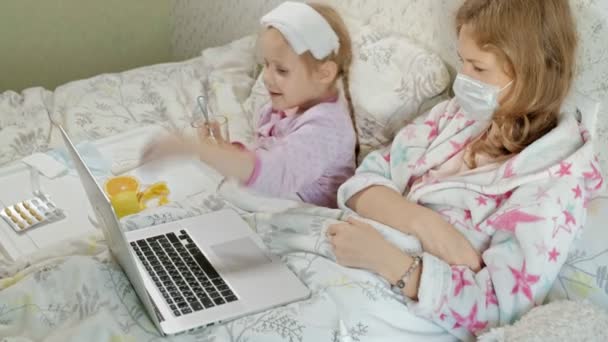 Ziek meisje met een temperatuur. Kind met koorts is liggend in bed met haar moeder, eten van fruit en met behulp van een laptop. — Stockvideo