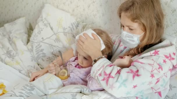 Sick girl with a temperature. Child with fever is lying in bed with her mother, eating fruit and using a laptop. — Stock Video