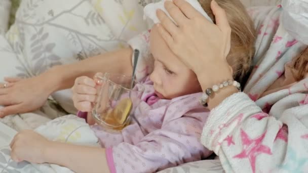 Ragazza malata con la febbre. Bambino con febbre è sdraiato a letto con la madre, mangiare frutta e utilizzando un computer portatile . — Video Stock