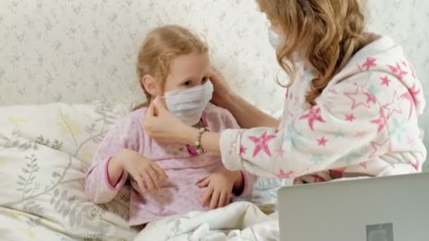 Krankes Mädchen mit einer Temperatur. Kind mit Fieber liegt mit Mutter im Bett, isst Obst und benutzt Laptop. — Stockvideo