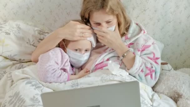 Menina doente com uma temperatura. Criança com febre está deitada na cama com a mãe, comendo frutas e usando um laptop . — Vídeo de Stock