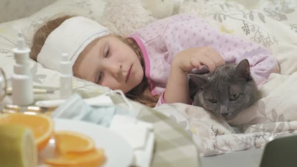 温度と病気の女の子。発熱児は猫とベッドで横になっています。. — ストック動画