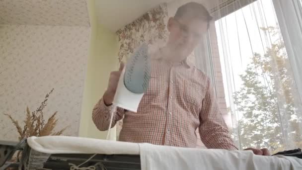 Un uomo accarezza la camicia sull'asse da stiro in casa sua — Video Stock