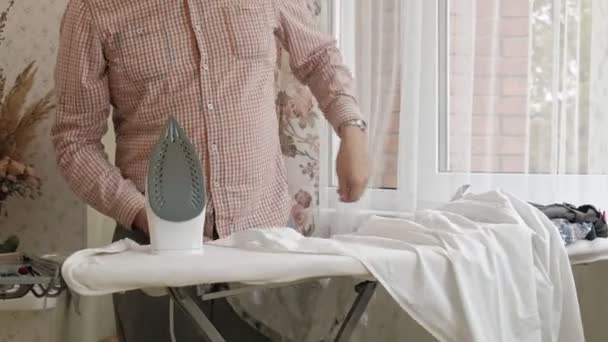 Un hombre acaricia su camisa en la tabla de planchar de su casa — Vídeos de Stock