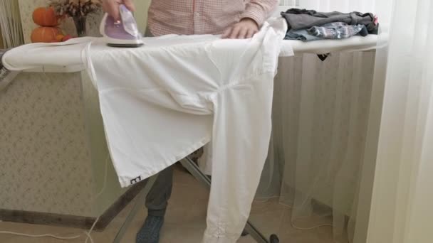 A man strokes his shirt on the ironing board in his house — Stock Video